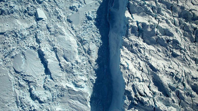 An aerial view of an ice cliff on Helheim Glacier (right side of the image) taken during NASA's Operation Icebridge in May, 2017. Shown at left is a mélange of ice pieces that have calved off the glacier and are now floating in the water - photo © NASA