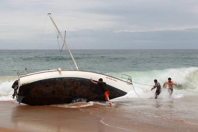 A group of bystanders attempt, unsuccessfully, to manoeuvre the yacht back into the water at Stanwell Park Beach on Sunday.  © Sylvia Liber
