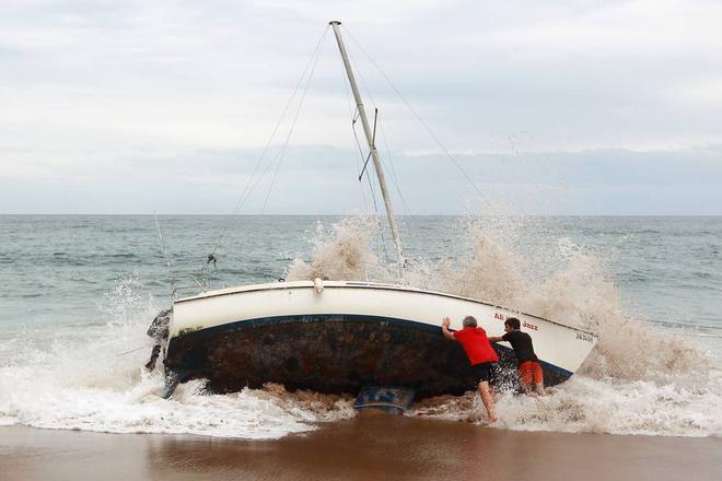A group of bystanders attempt, unsuccessfully, to manoeuvre the yacht back into the water at Stanwell Park Beach on Sunday.  © Sylvia Liber