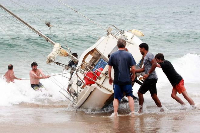 A group of bystanders attempt, unsuccessfully, to manoeuvre the yacht back into the water at Stanwell Park Beach on Sunday.  © Sylvia Liber