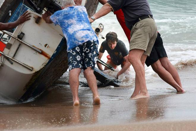 A group of bystanders attempt, unsuccessfully, to manoeuvre the yacht back into the water at Stanwell Park Beach on Sunday.  © Sylvia Liber
