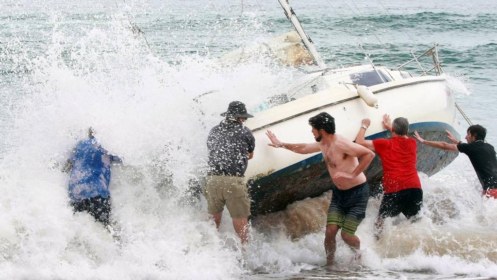 A group of bystanders attempt, unsuccessfully, to manoeuvre the yacht back into the water at Stanwell Park Beach on Sunday.  © Sylvia Liber