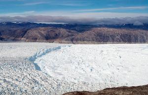 The ridge of ice is the terminus of Helheim Glacier, where it flows into the ocean. To the right of the ridge, the fjord is covered by a thick melange of floating icebergs and sea ice. That makes the region near the glacier's terminus inaccessible by boat. On the mountains in the background, you can see a ``bathtub ring`` indicating the prevoius extent of the glacier before it had thinned and retreated in recent years. photo copyright Woods Hole Oceanographic Institution (WHOI) http://www.whoi.edu/ taken at  and featuring the  class