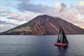 The Polish crewed VO65 Wind Whisper passes the active volcano that is Stromboli during the 2025 race &copy; Kurt Arrigo / Rolex